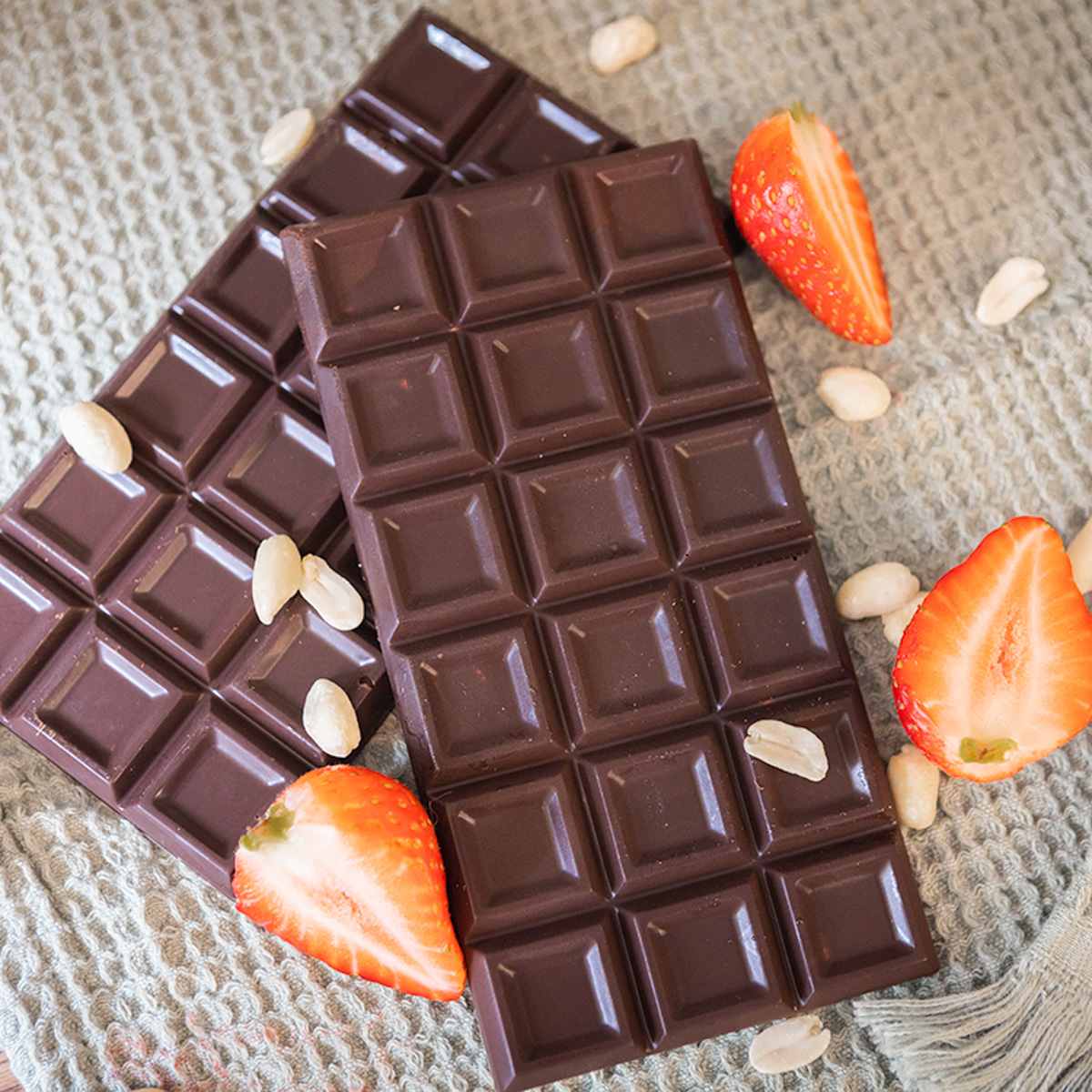 Two bars of chocolate with pieces of strawberries and nuts scattered around.