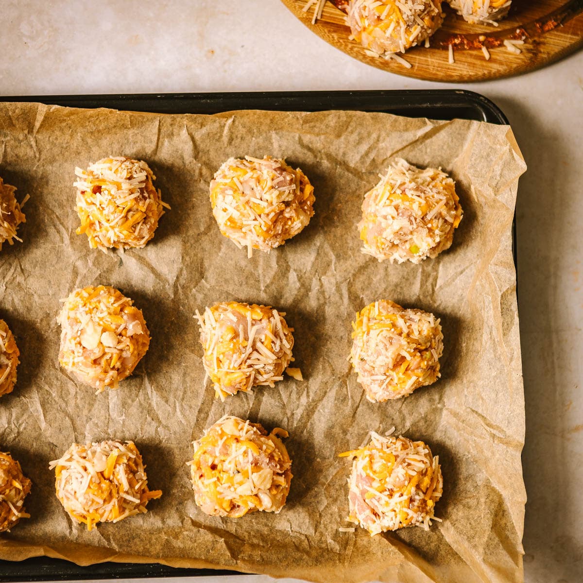 Uncooked chicken meatballs on a lined baking tray.