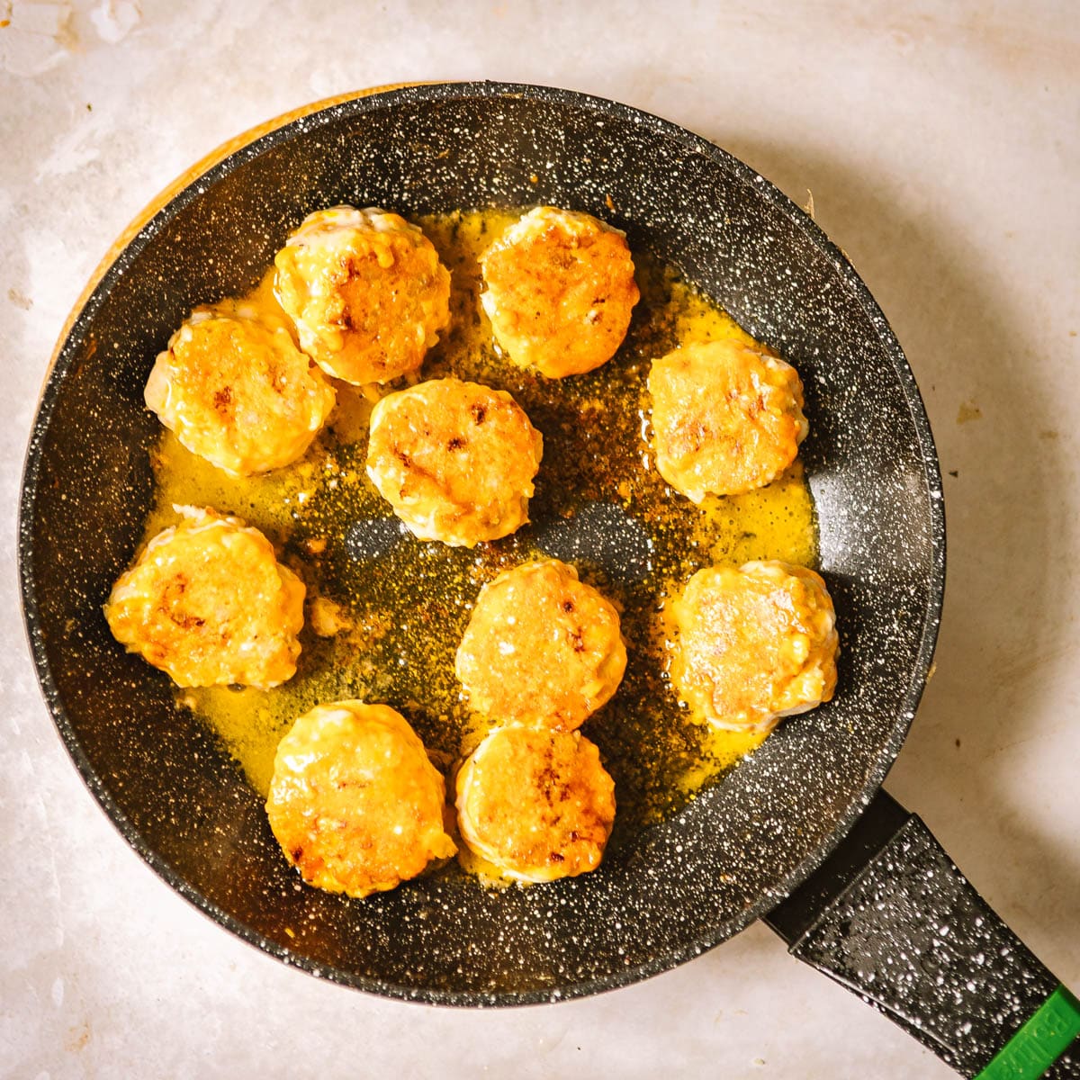 Chicken meatballs being fried on a black skillet.