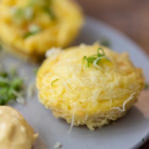 Two egg muffins on a plate with mayonnaise and spring onions.