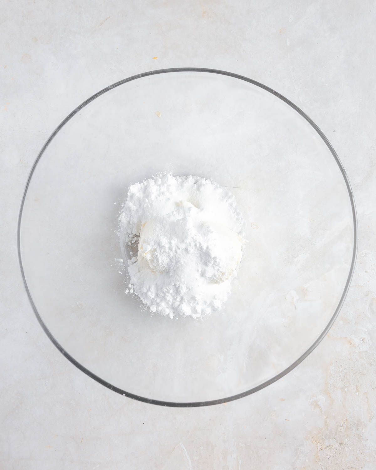 A clear bowl with white powdered ingredients inside.