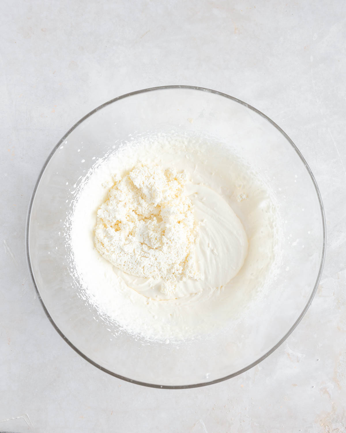 A clear bowl with mixed cream cheese and curd added on top.