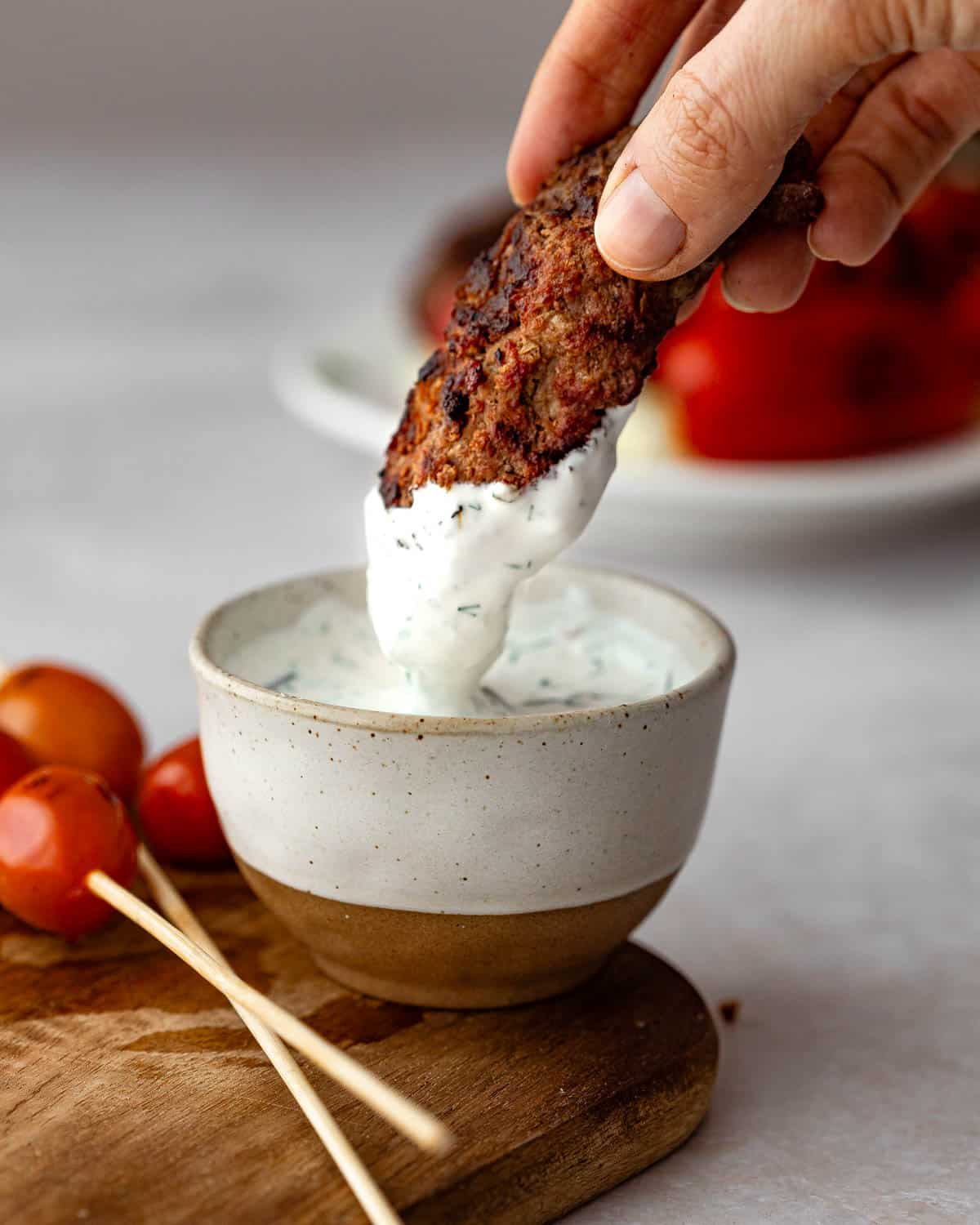 A grilled beef kebab being dipped in a sour cream dipping sauce.