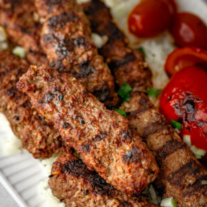 Beef kebabs on a white plate, served with white rice and grilled bell pepper.