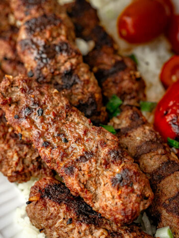 Beef kebabs on a white plate, served with white rice and grilled bell pepper.
