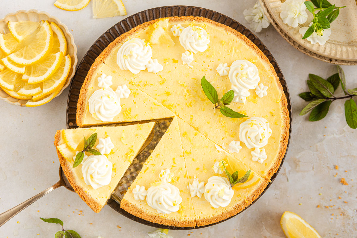 An overhead shot of a round lemon tart with a slice being taken out.