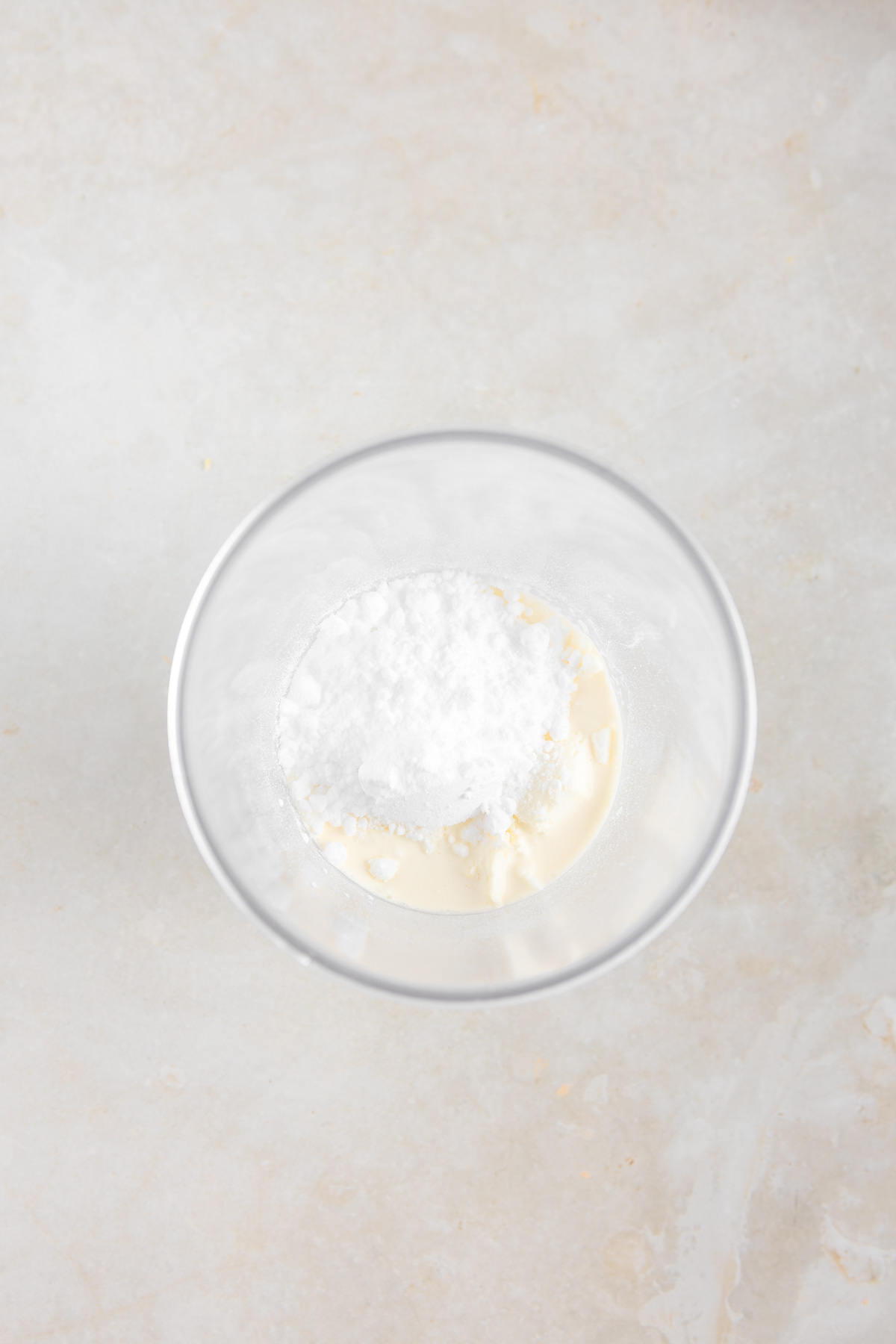 A round transparent bowl with cream cheese and sweetener to be mixed.