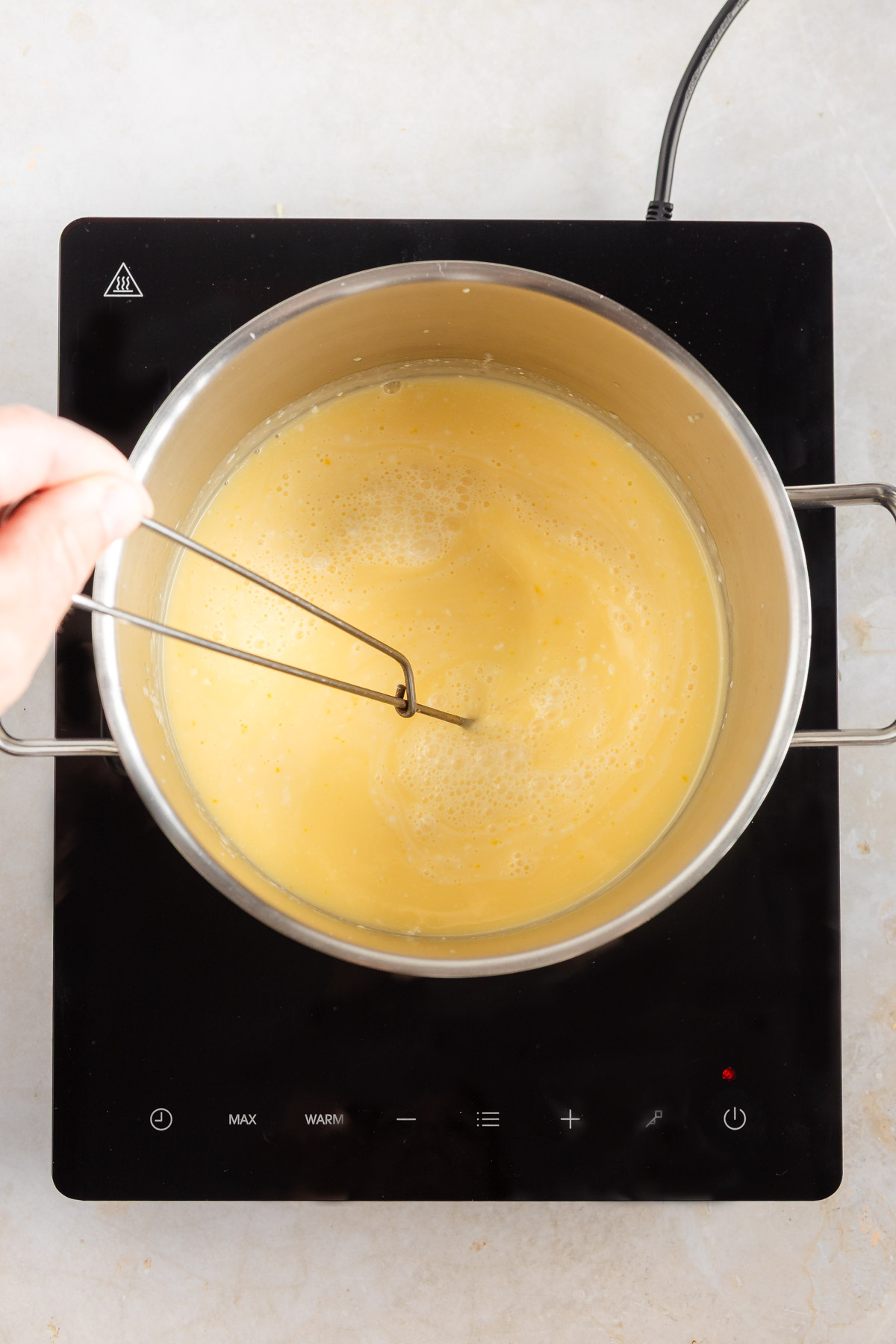 A round pot on a portable stove, with lemon cream being heated while stirring.