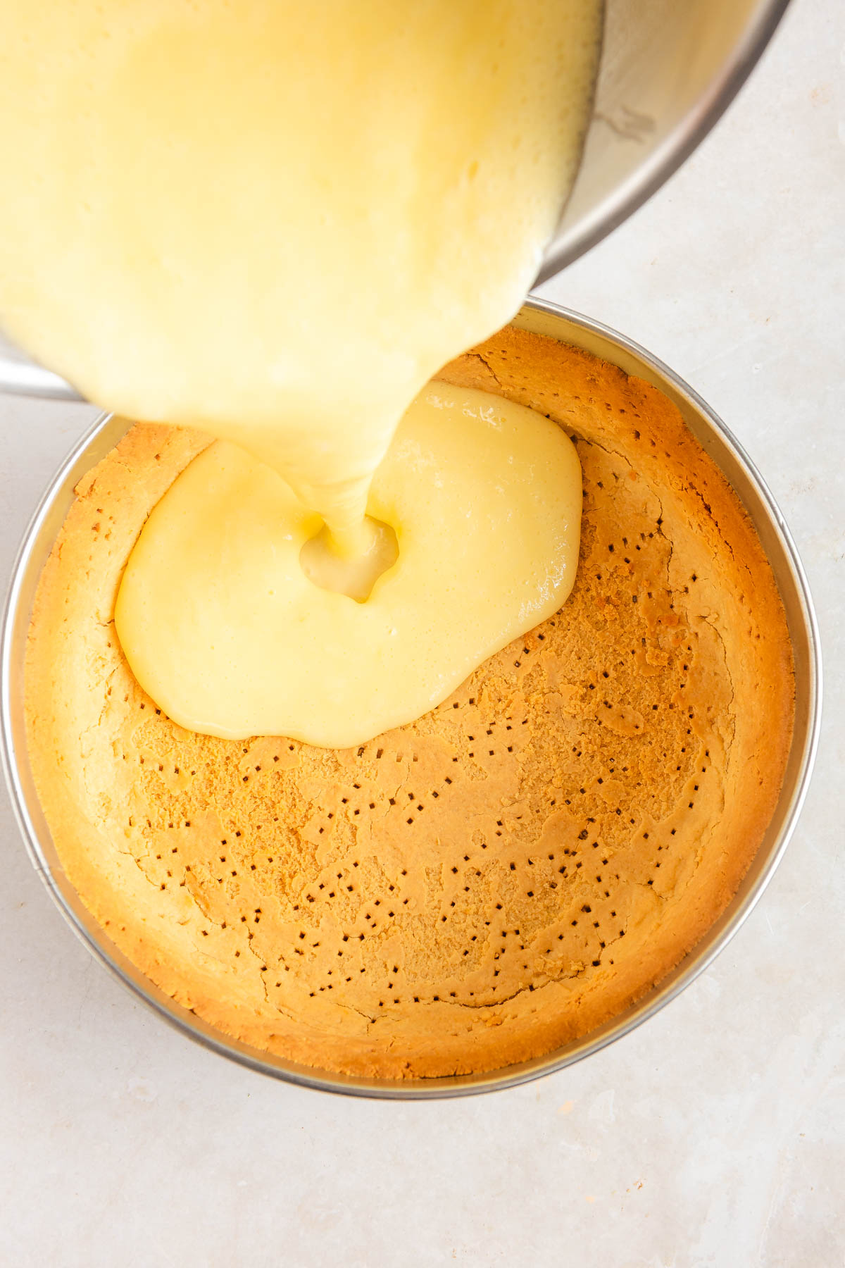 Lemon cream being poured over the base layer of lemon mousse tart.