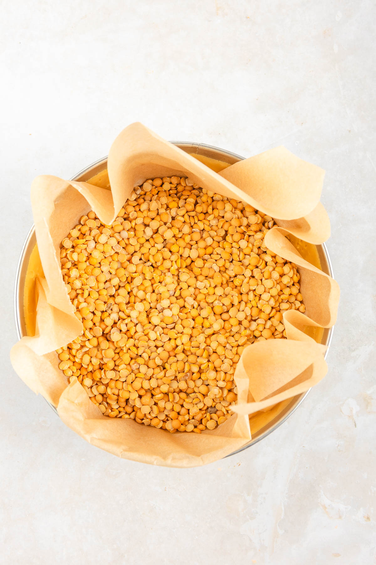 Round baking springform with a parchment paper and peas on top.