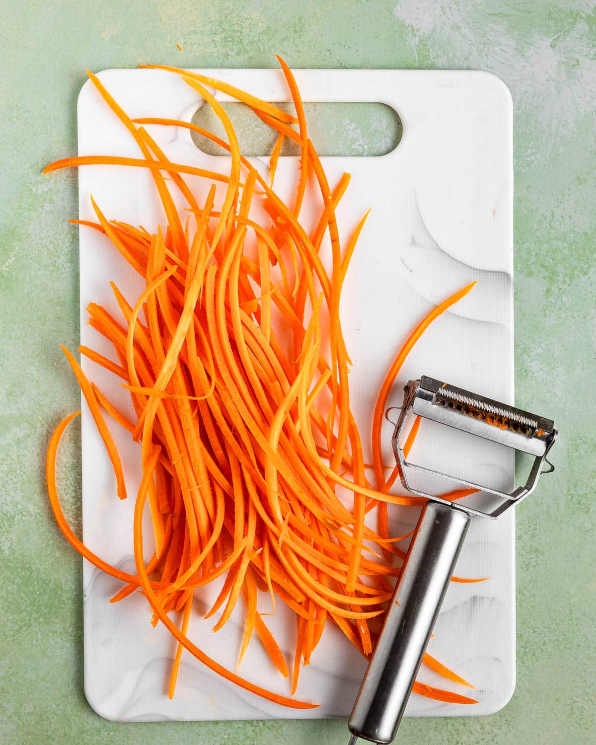 A white cutting board with shredded carrot.