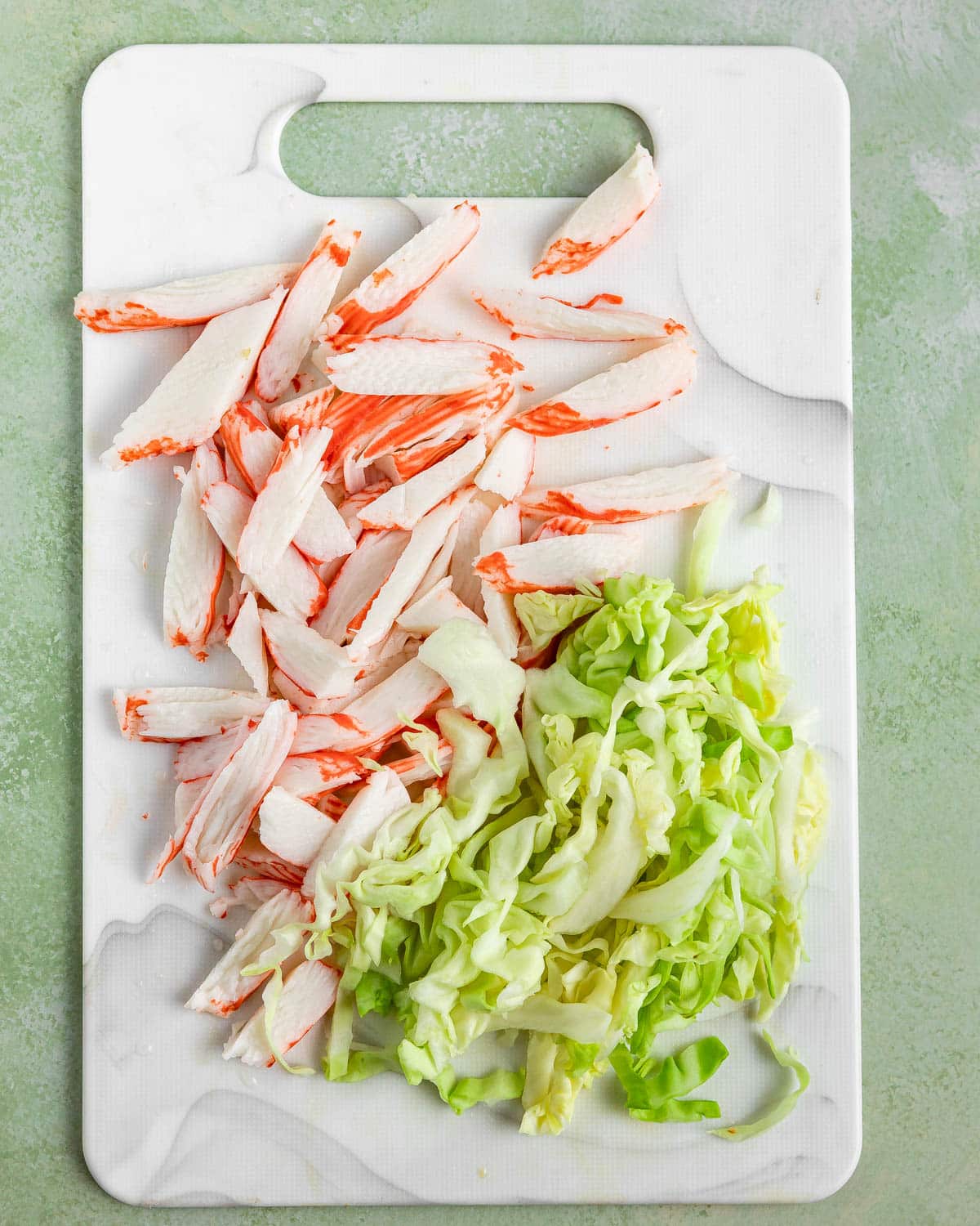 A cutting board with cut surimi crab sticks and chopped cabbage.