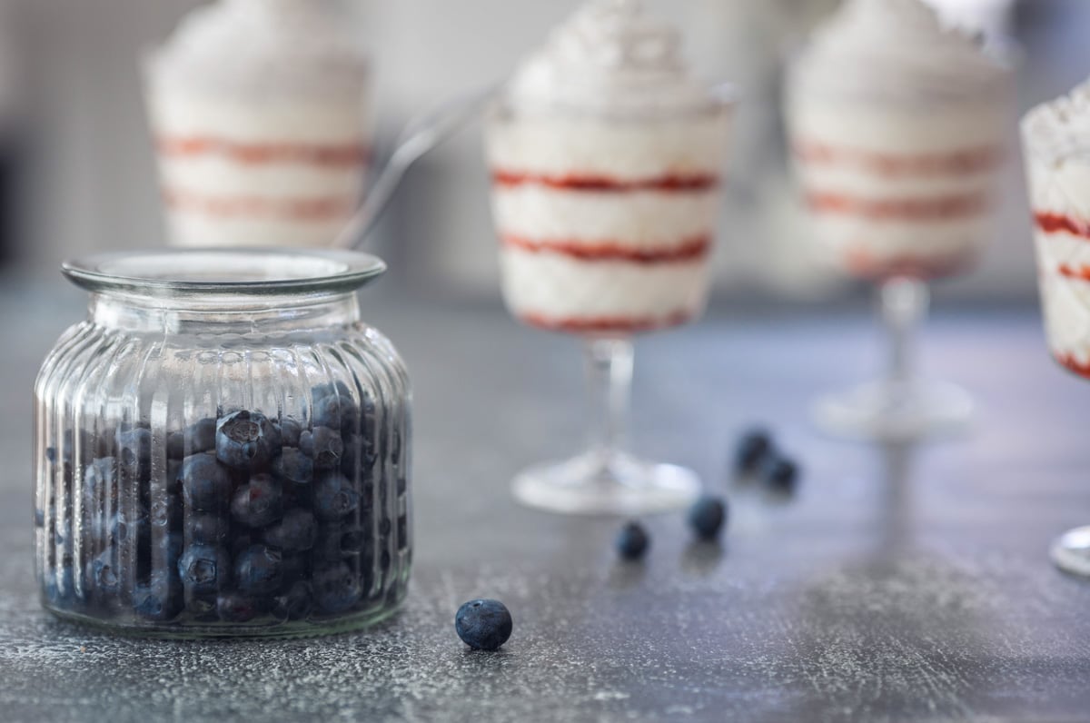 Glasses with white and red dessert and blueberries scattered.