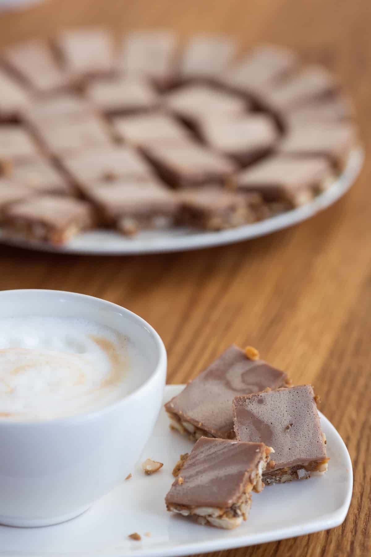Cookies with nuts and chocolate on a plate besides a cup of coffee.