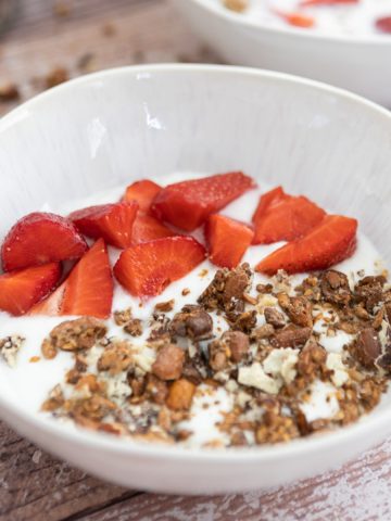 A white bowl with granola and strawberries with milk in it.