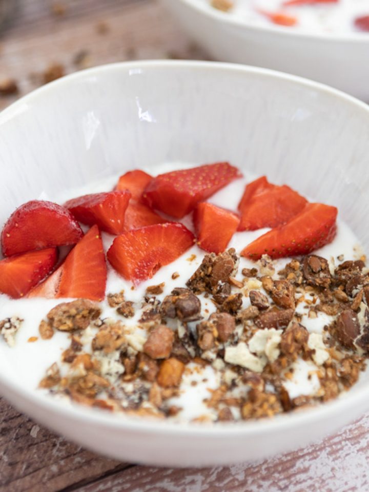 A white bowl with granola and strawberries with milk in it.