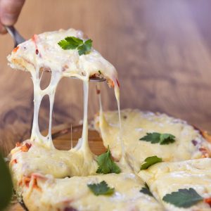 A pizza with cheese and parsley on top, on a wooden table, one slice lifted.