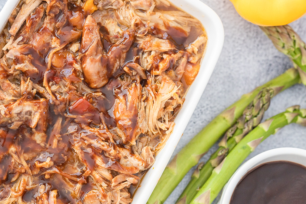 Pulled pork in a baking pan with asparagus on the side.