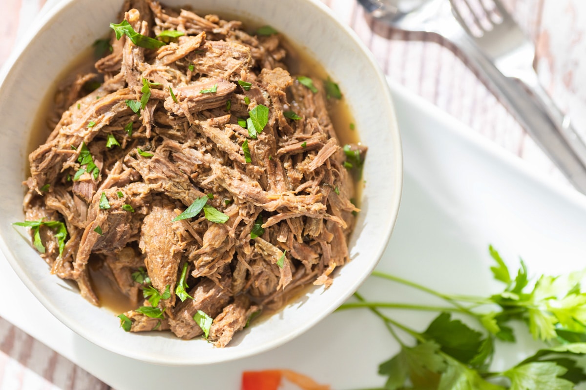 A white plate with shredded beef and parsley.