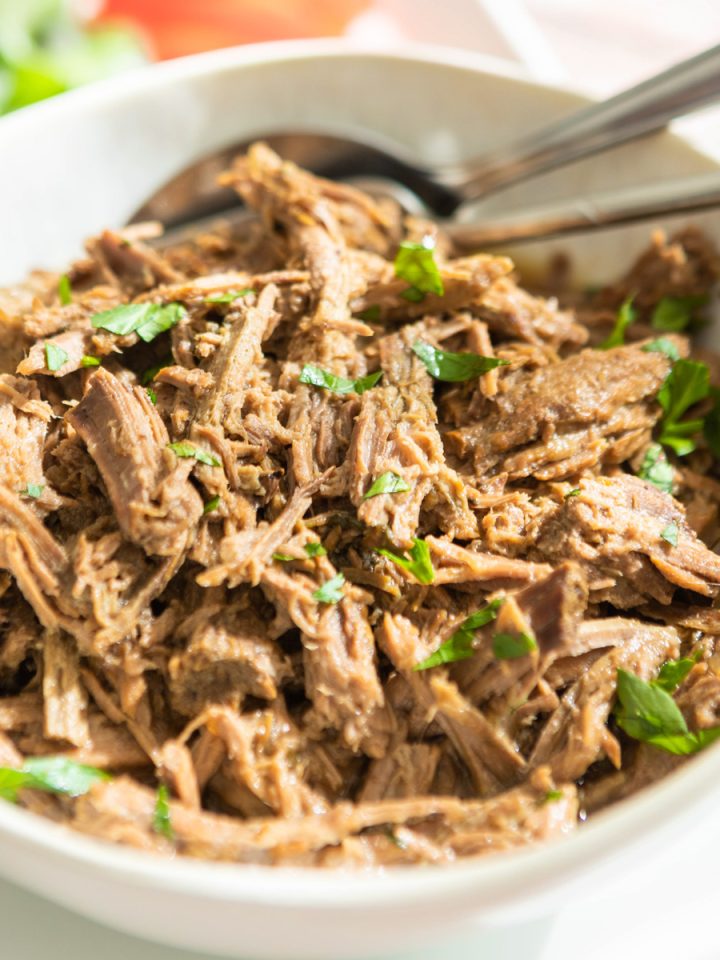 A white plate with shredded beef and parsley.