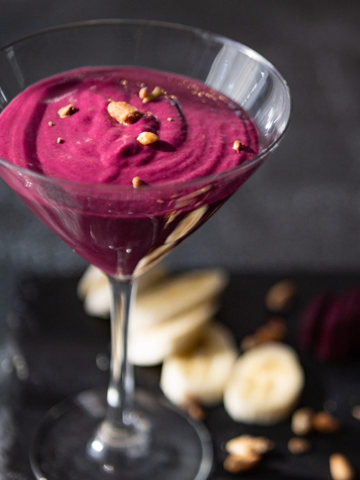 A glass with purple smoothie, sprinkled with nuts, on a dark background.