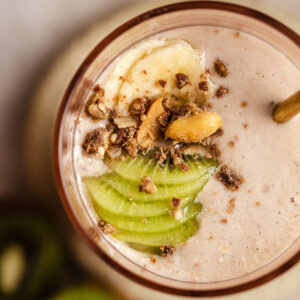 View from above onto a glass filled with banana oat smoothie, decorated with fresh fruit slices.
