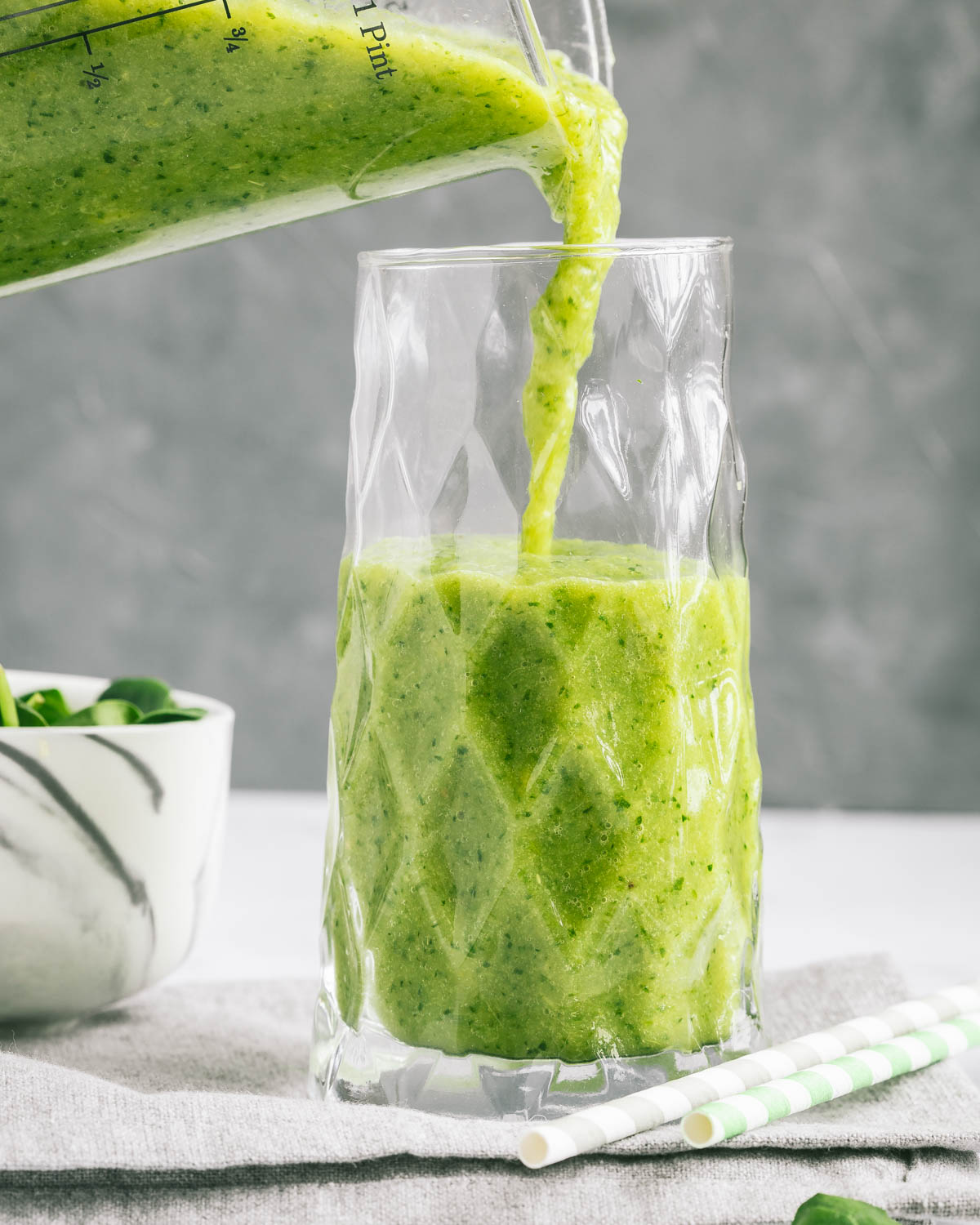 Green spinach smoothie being poured into a tall glass.