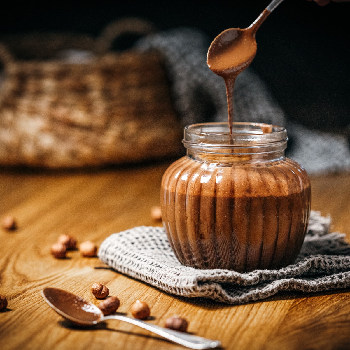 A jar with brown chocolate cream and a spoon pouring the cream into the jar.
