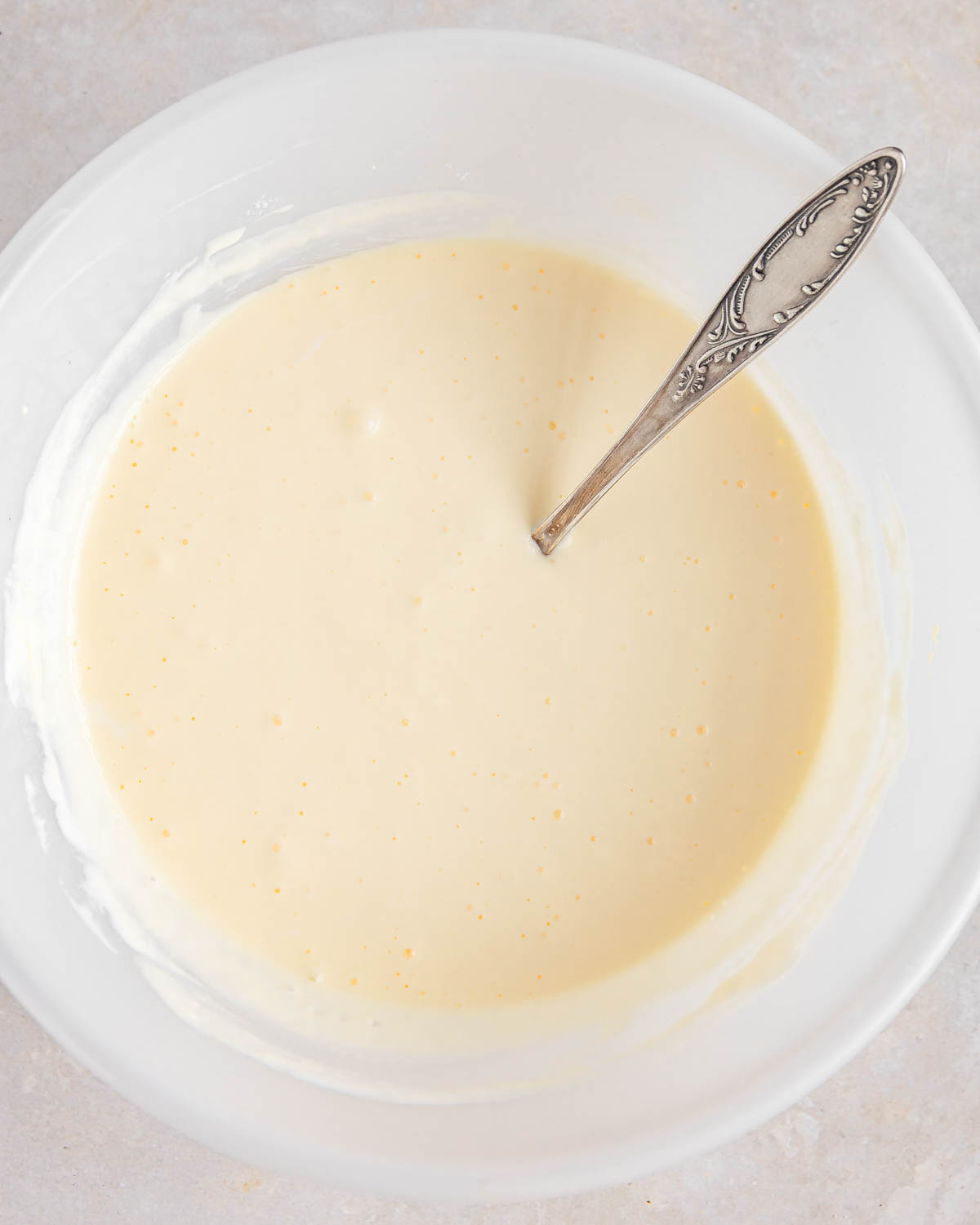 A light bowl with a cream mixture and a spoon submerged.
