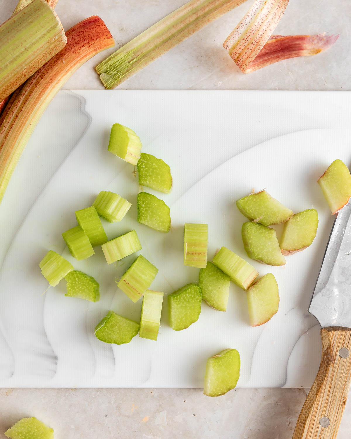 The process of cutting rhubarb on a white cutting board.