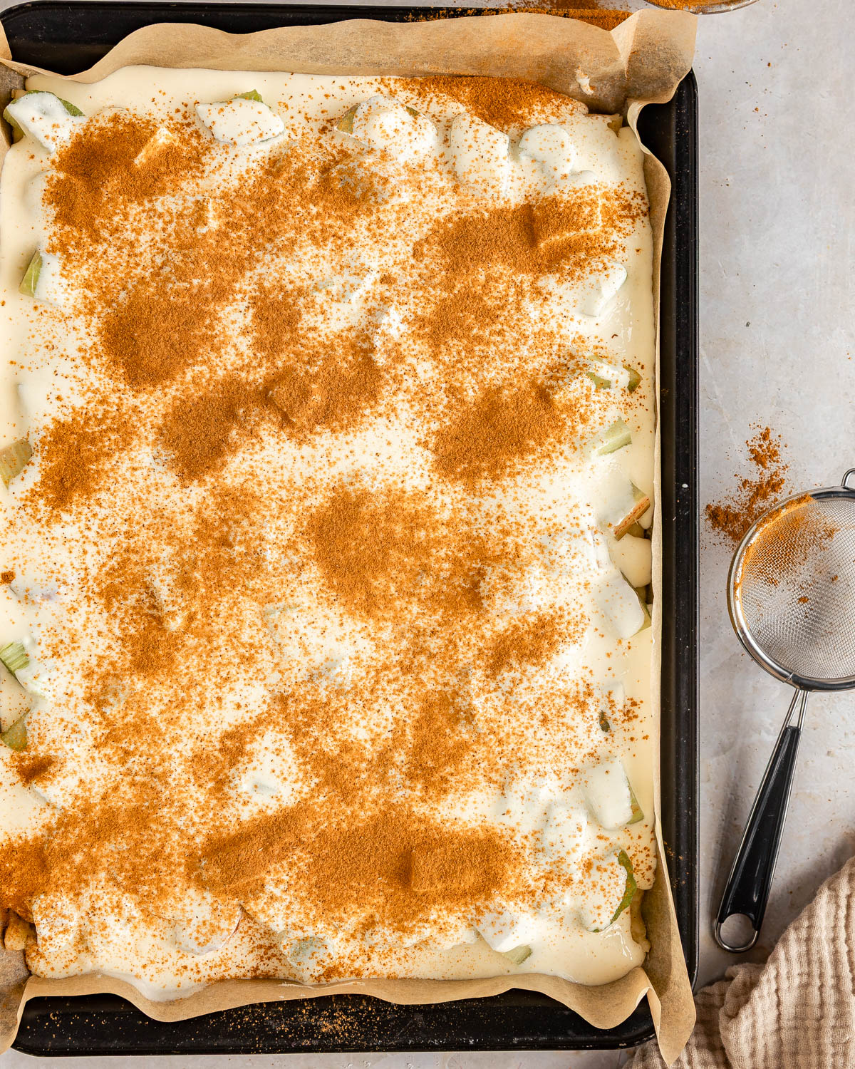 Unbaked rhubarb sheet pan cake, with cinnamon sprinkled on top.