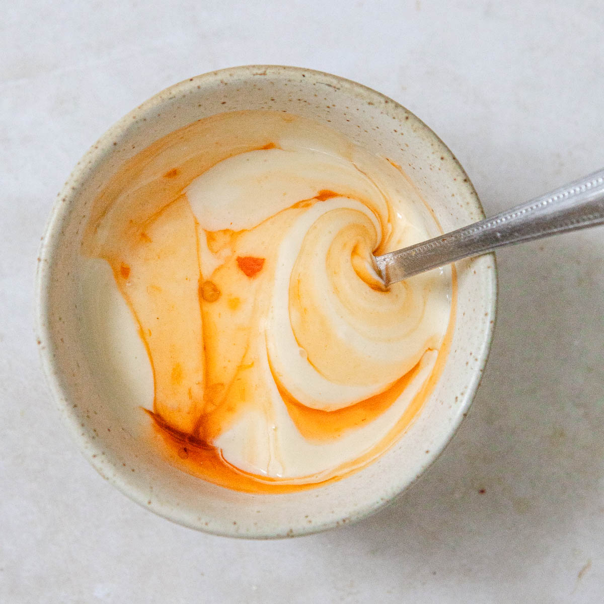 A small round bowl with mayo and red chili sauce.