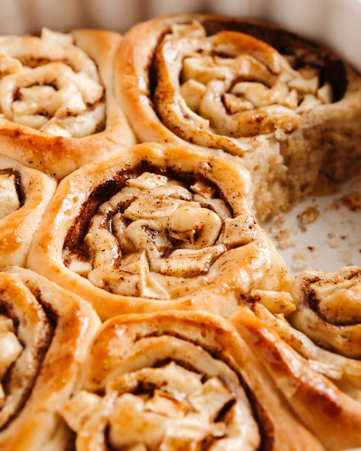 A closeup shot of baked apple cinnamon brioche rolls in a baking dish with one roll taken out.
