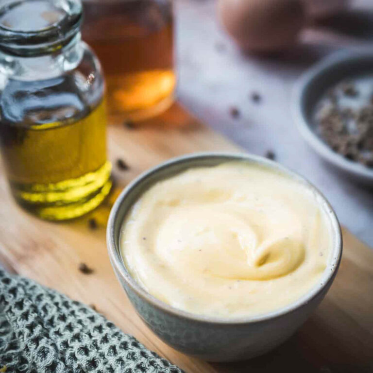 A bowl of mayonnaise, small bottles of oil and some spices on a kitchen countertop.