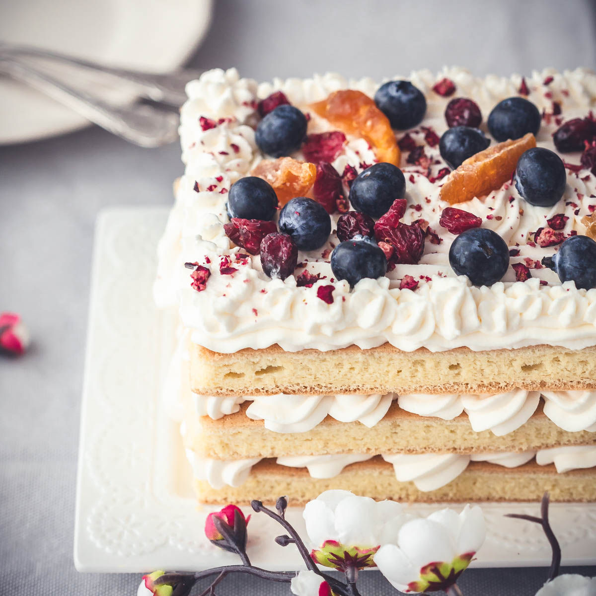 A layered cake with fruit and berry topping, served on a white rectangular plate.