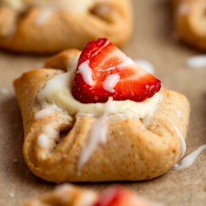 A closeup shot of a sugar-free Danish pastry with drizzled glaze and topped with a fresh strawberry slice.