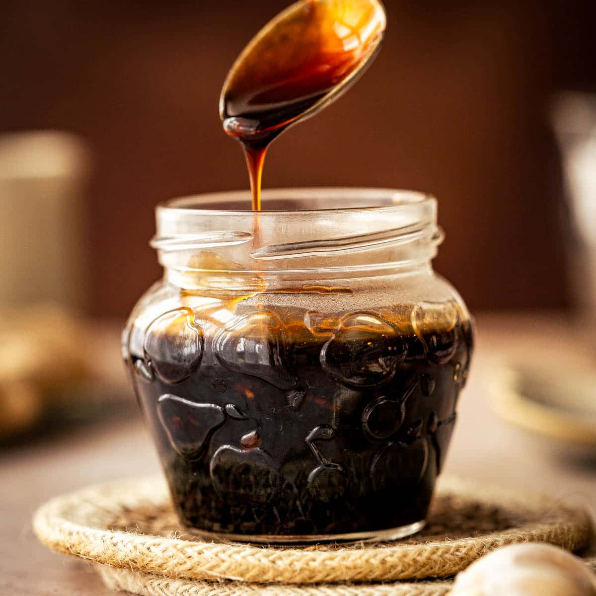 A side view on a glass jar with teriyaki sauce and a spoon being raised from it.