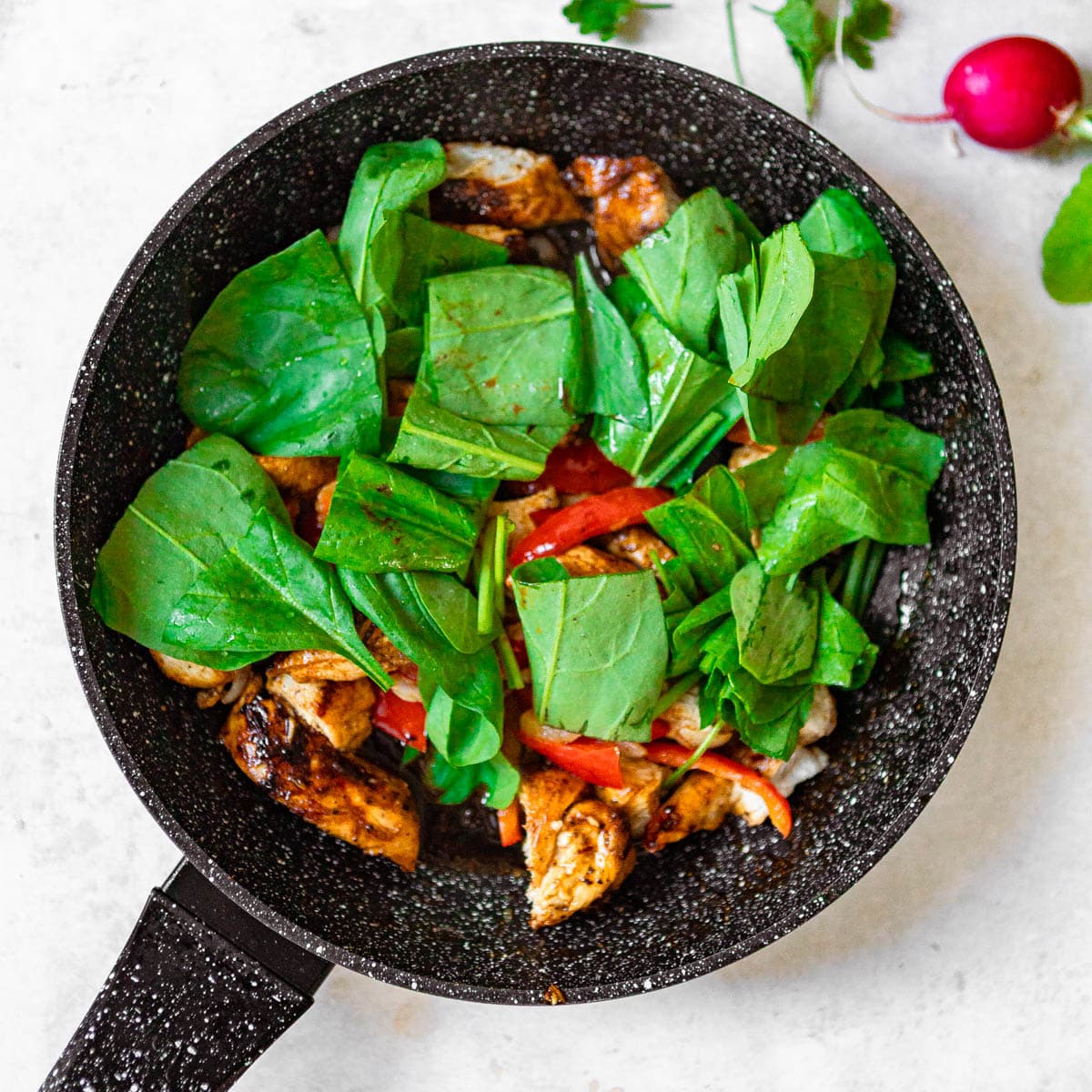 A skillet with fried chicken, veggies, topped with bright green spinach leaves.