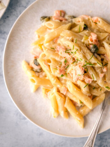 A plate with smoked salmon pasta, served on a pale blue table.