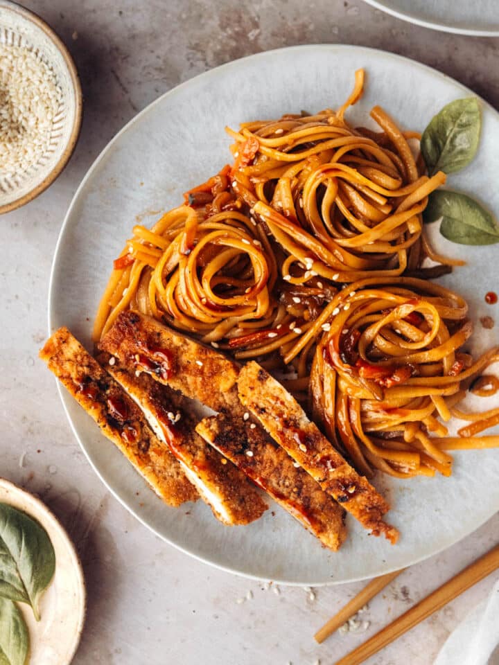 Stir-fry teriyaki noodles served with sliced pork chops on a white plate, view from the top.