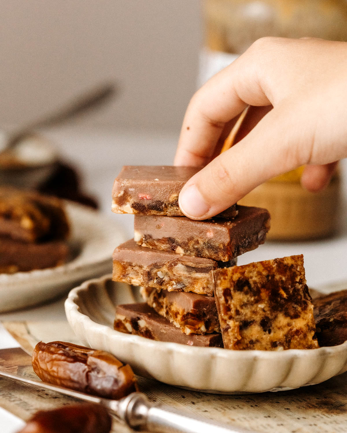 A side view of stacked sugar-free date barks and a child's hand picking the top piece.