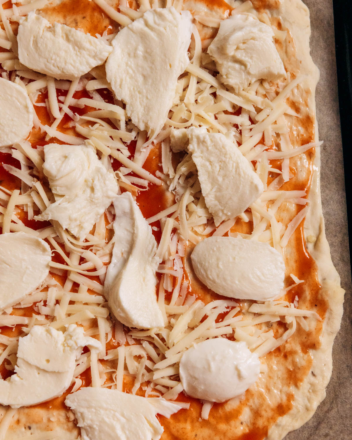 An uncooked homemade pizza with grated cheese and mozzarella on top.
