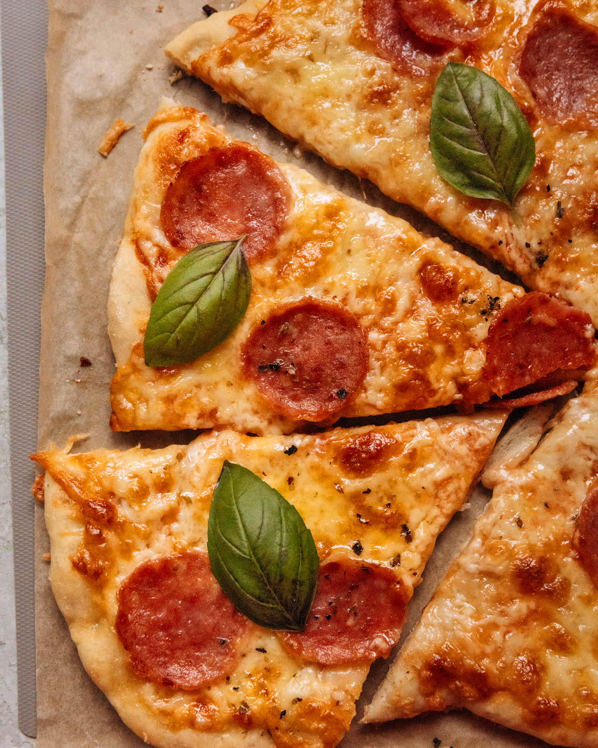 A top-down view of a sliced pizza with cheese, pepperoni, and fresh basil.