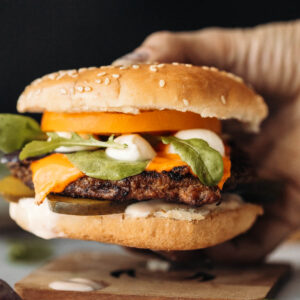 A side view of a hand holding a pork chop burger.