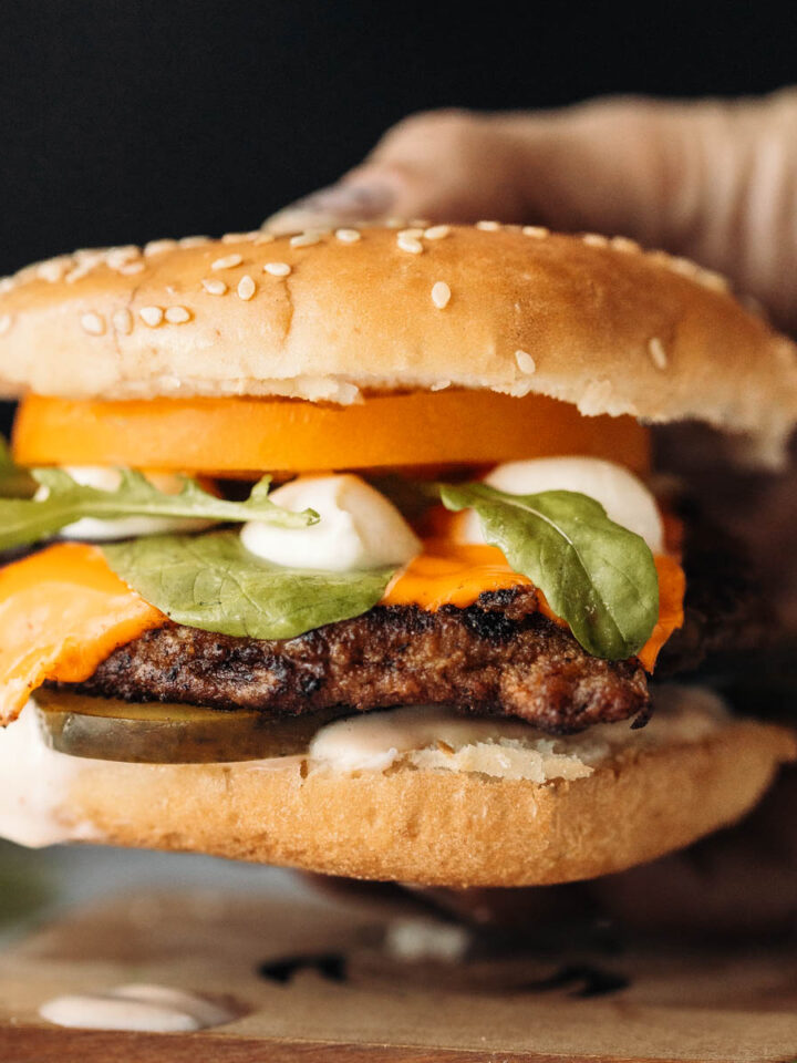 A side view of a hand holding a pork chop burger.