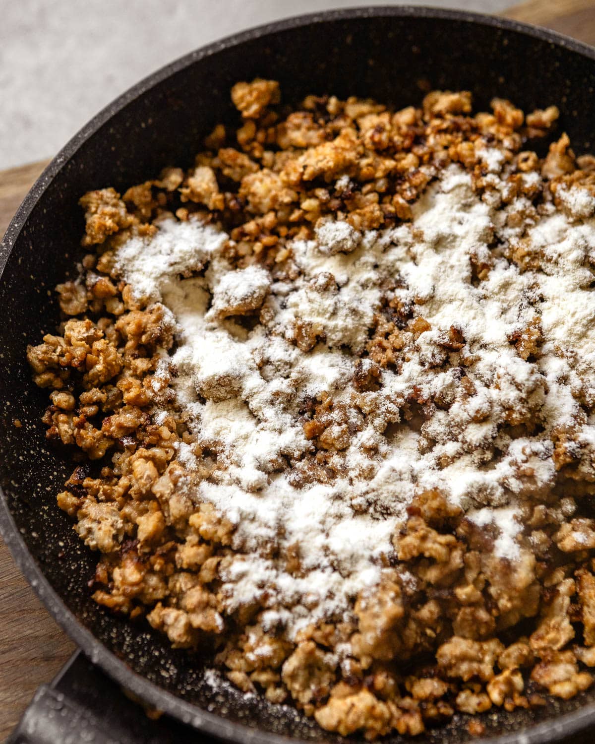Minced meat in a skillet with flour sprinkled on top.