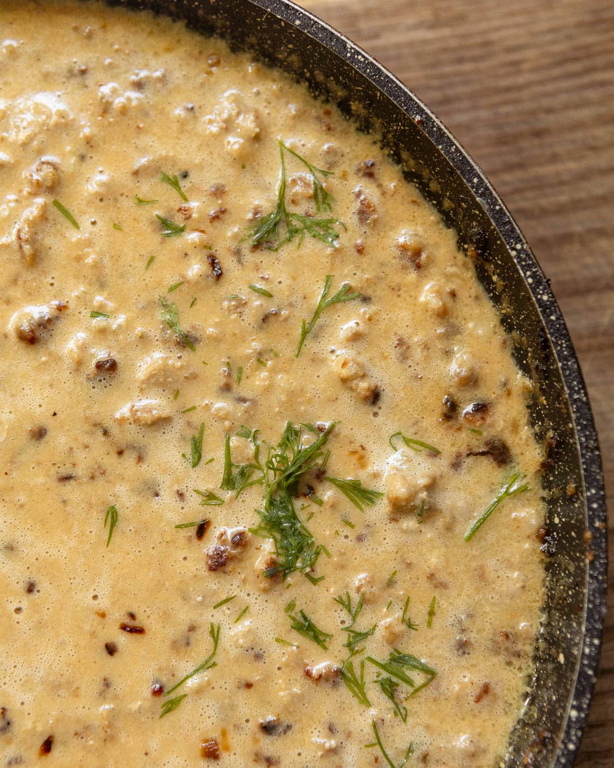 Minced meat sauce in a skillet with fresh herbs sprinkled on top.