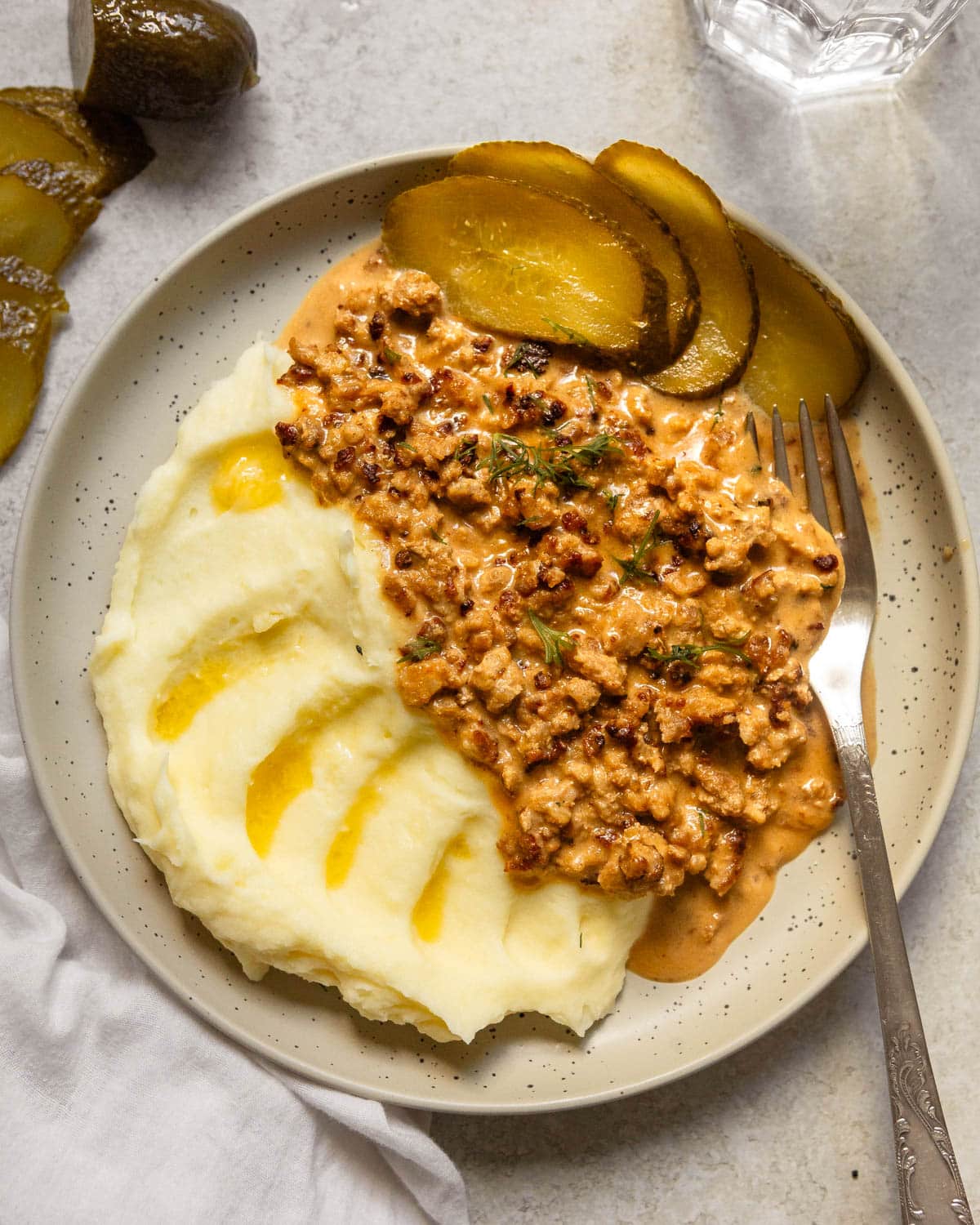 A serving of minced meat sauce with mashed potatoes and sliced pickle on the side.