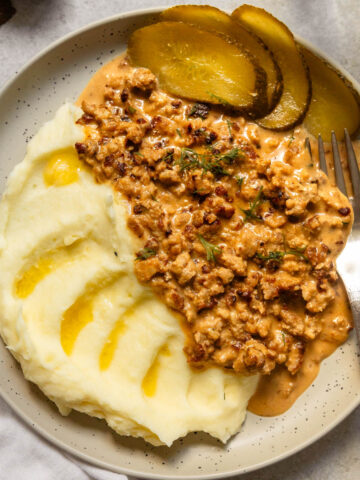 A serving of minced meat sauce with mashed potatoes and sliced pickle on the side.