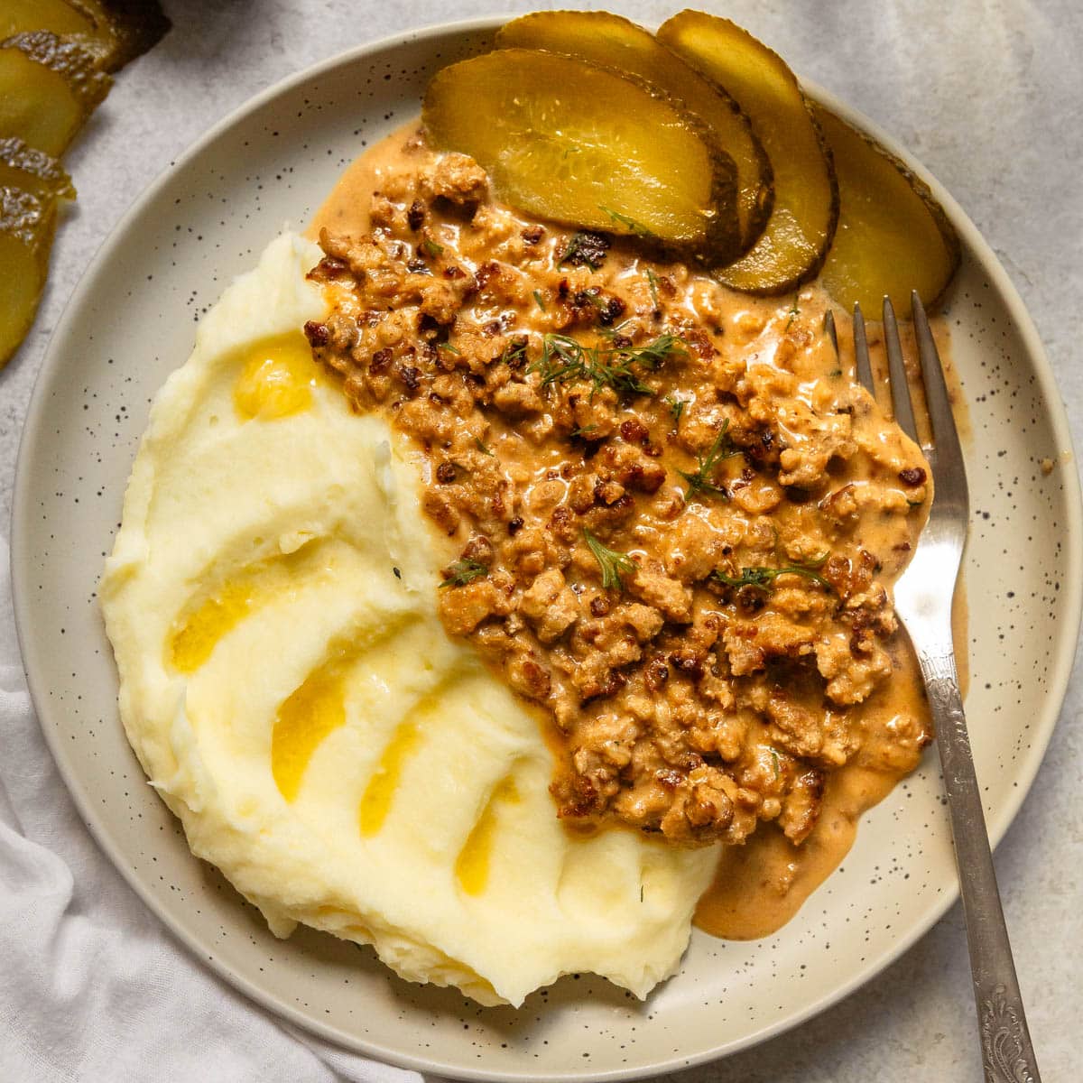 A serving of minced meat sauce with mashed potatoes and sliced pickle on the side.